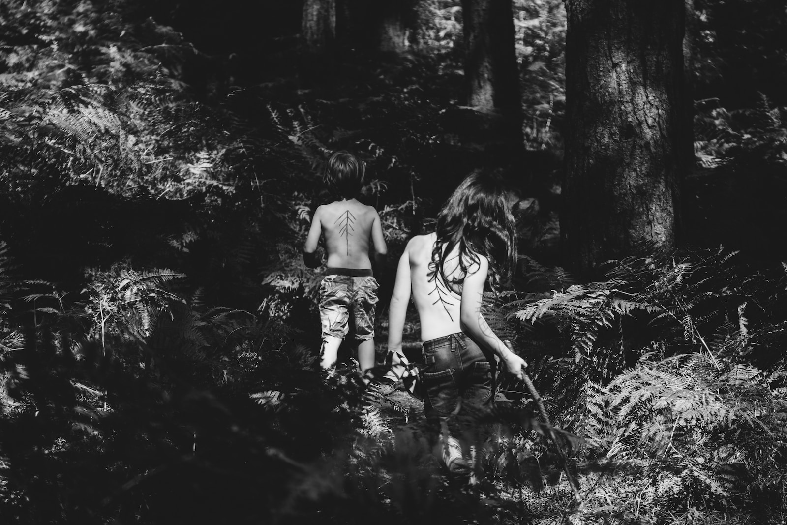 grayscale photography of two topless persons standing at the forest during day